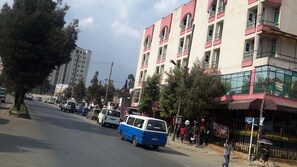 A street with a blue and white van parked on the side, buildings with balconies, and pedestrians. - SGS Hotel (Addis Ababa)