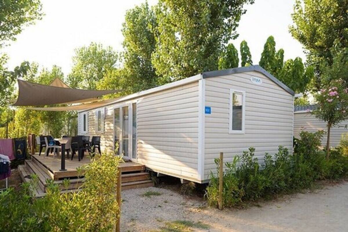 A single-story mobile home with a covered patio area, outdoor seating, and a small deck.