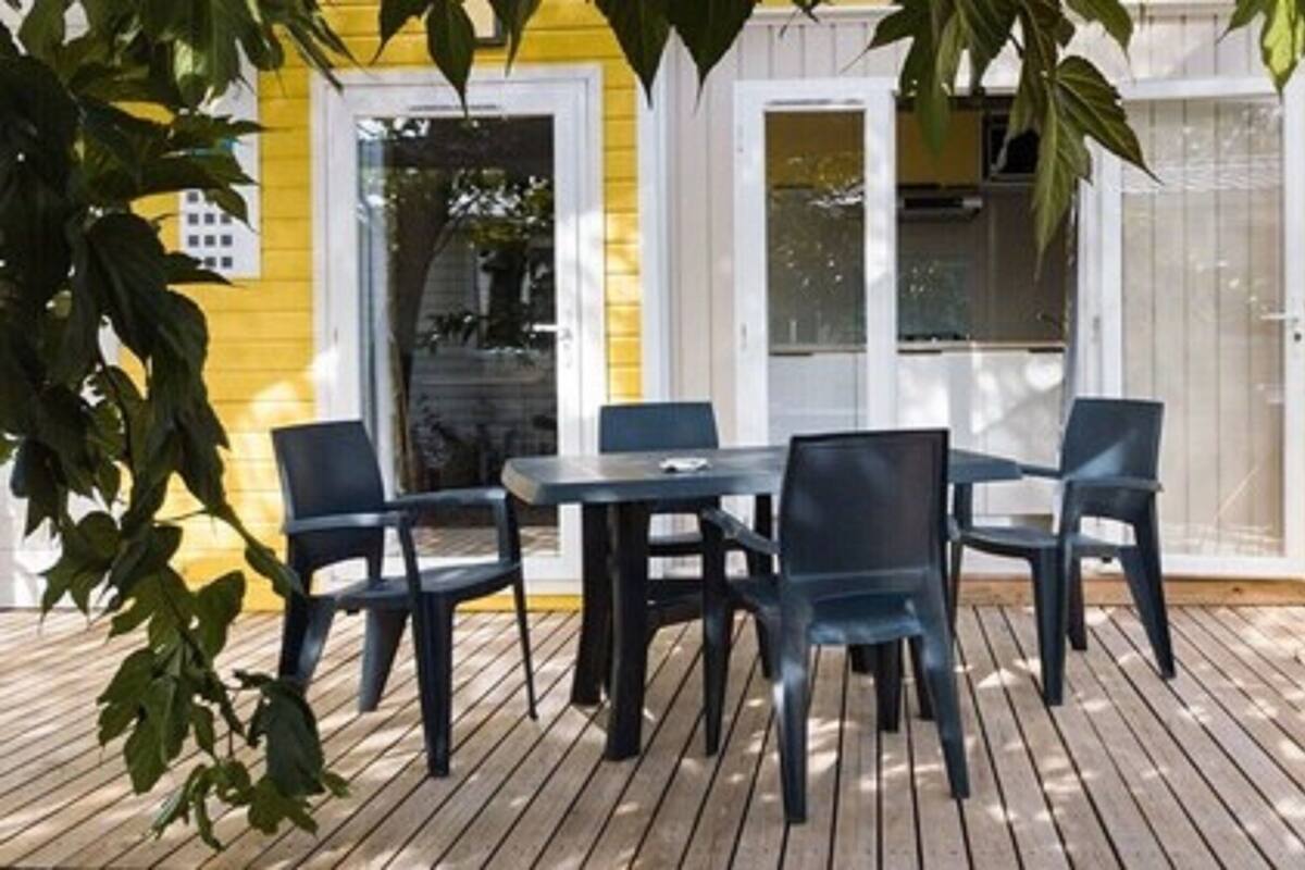 A wooden deck with a table and chairs, a yellow building in the background, and a wooden fence.