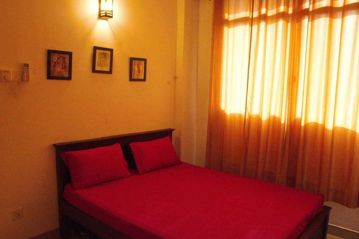 A room with a bed, a wall-mounted light, and three framed pictures.
