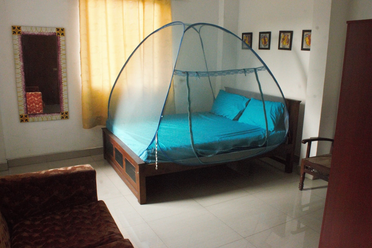 A bedroom with a bed under a mosquito net, a chair, and a mirror on the wall.