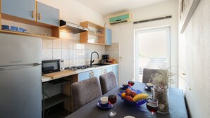 Une cuisine moderne équipée d’un réfrigérateur Koncar, d’un four à micro-ondes et d’une cuisinière à gaz. On y trouve une table à manger avec des chaises et un vase contenant des fleurs séchées.