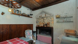 Une cuisine rustique avec une cheminée en pierre, des étagères en bois et une nappe à carreaux.