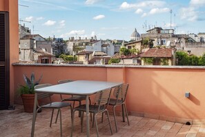 A rooftop terrace with a table and chairs, overlooking a cityscape with historic buildings and a dome structure.