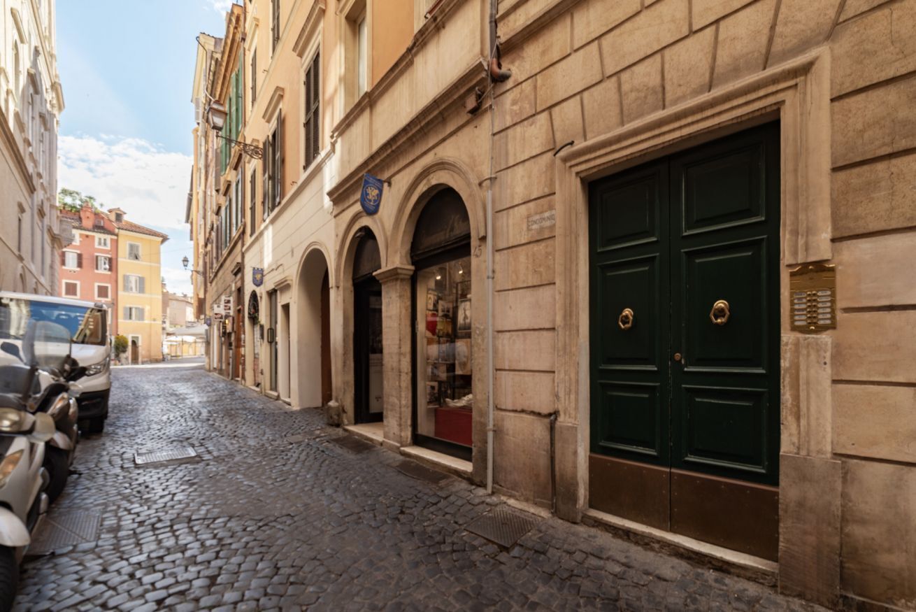 Una calle adoquinada con edificios históricos, una puerta doble verde y scooters estacionados.