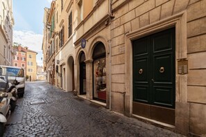 A cobblestone street with historic buildings, a green double door, and parked scooters.