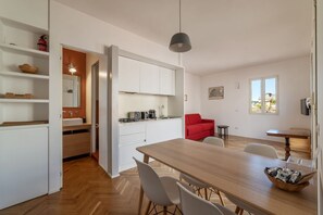A modern kitchen with white cabinets, a wooden dining table, and a red chair.