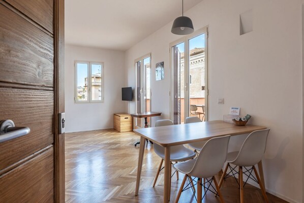 A modern kitchen with a wooden table and chairs, a television, and a view of buildings outside.