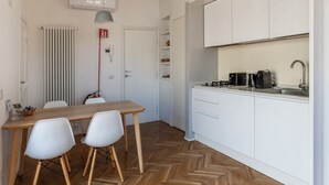 A modern kitchen with white cabinets, a wooden dining table, and two white chairs. - Modern studio with panoramic terrace, by Campo de’ Fiori - Wifi, Independent Heating, A/C (Roma)