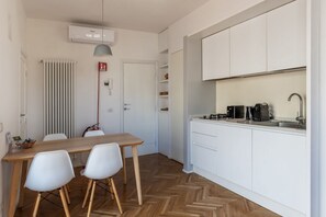 A modern kitchen with white cabinets, a wooden dining table, and two white chairs. - Modern studio with panoramic terrace, by Campo de’ Fiori - Wifi, Independent Heating, A/C (Roma)