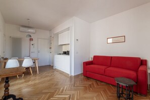 A modern living room with a red sofa, wooden herringbone flooring, a dining area with a wooden table and white chairs, and a kitchen area with white cabinets. - Modern studio with panoramic terrace, by Campo de’ Fiori - Wifi, Independent Heating, A/C (Roma)