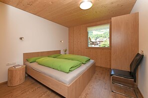 A wooden-paneled room with a bed, a chair, a small round table, and a window with a view. - Haus Bianca - Apartment 2-8 pers. (Schoppernau)