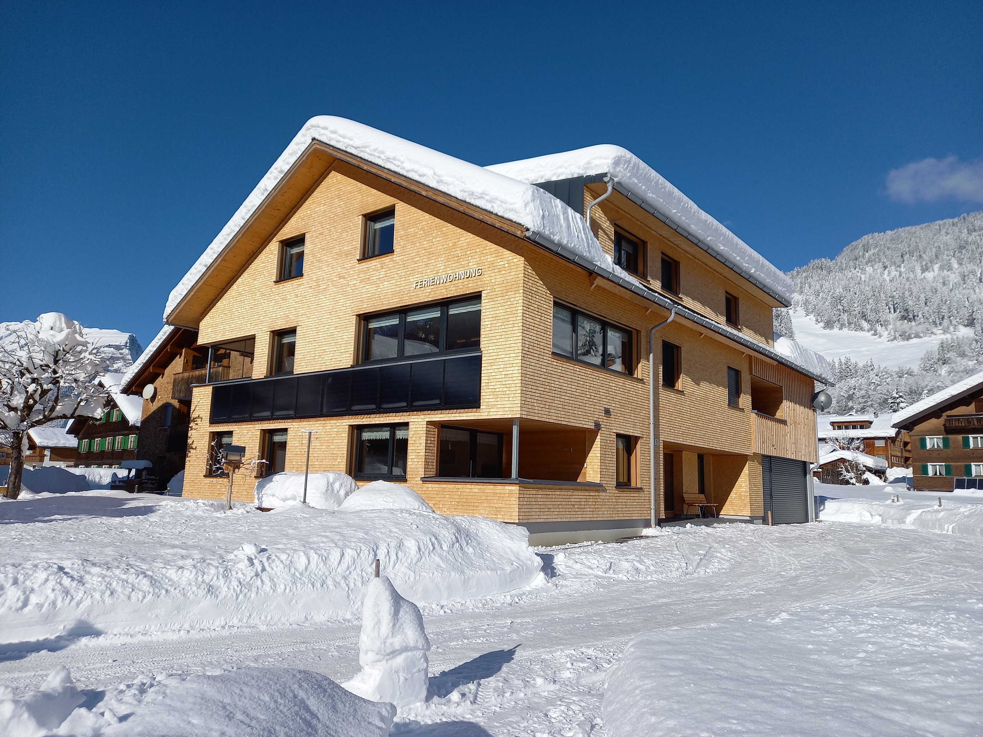 A multi-story building with a prominent balcony, surrounded by snow-covered terrain and mountains.