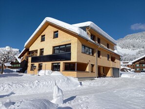 Un immeuble à plusieurs étages doté d’un balcon imposant, entouré d’un paysage enneigé et de montagnes.