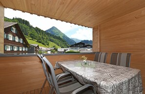 Un balcon en bois, agrémenté d’une table et de chaises, qui offre une vue sur un paysage montagneux parsemé de bâtiments traditionnels.