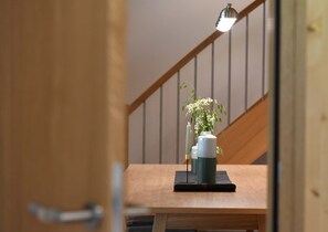 A wooden table with a vase of flowers and a candle, a wooden chair, and a staircase with a railing. - Haus Bianca - Apartment 2-8 pers. (Schoppernau)