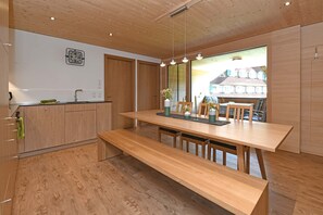 A modern kitchen with wooden cabinetry, a central island, and a dining area with benches. - Haus Bianca - Apartment 2-8 pers. (Schoppernau)