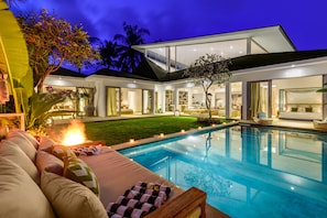 Una casa moderna con piscina, mobiliario exterior y un interior bien iluminado.