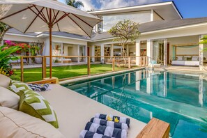 Un área moderna junto a la piscina con una tumbona, sombrilla y un borde de piscina ordenado.