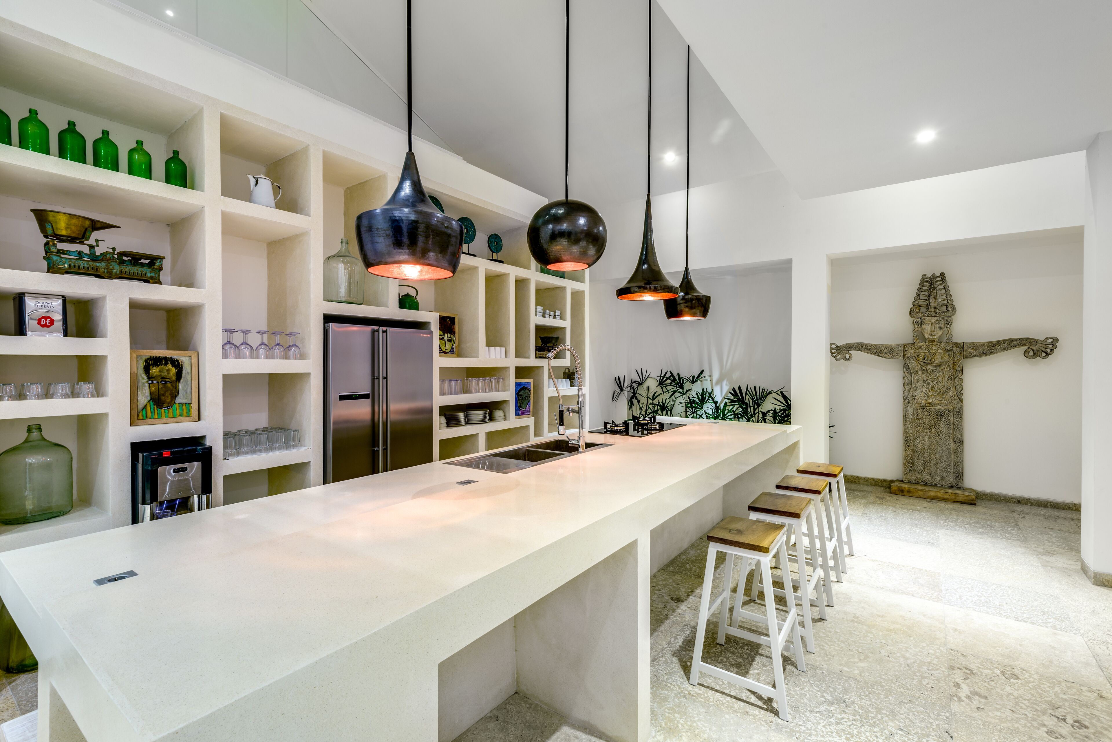 Una cocina moderna con una isla grande, taburetes de bar, lámparas colgantes y una estatua en la pared.