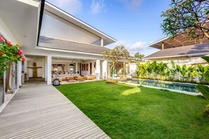 Una casa moderna con una amplia terraza, piscina y césped cuidado.