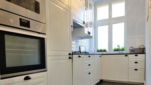 Eine Küche mit weißen Schränken, einem eingebauten Backofen, einer Pendelleuchte und einem Fenster mit Blick auf Grünflächen.