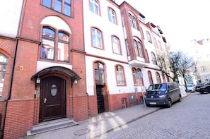 Traditional European-style building with arched and rectangular windows, a dark brown door, and steps leading to the entrance.