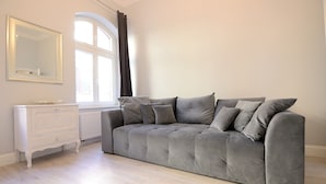 Ein neutral eingerichtetes Wohnzimmer mit grauem Sofa, einer weißen Kommode und einem großen Spiegel an der Wand.