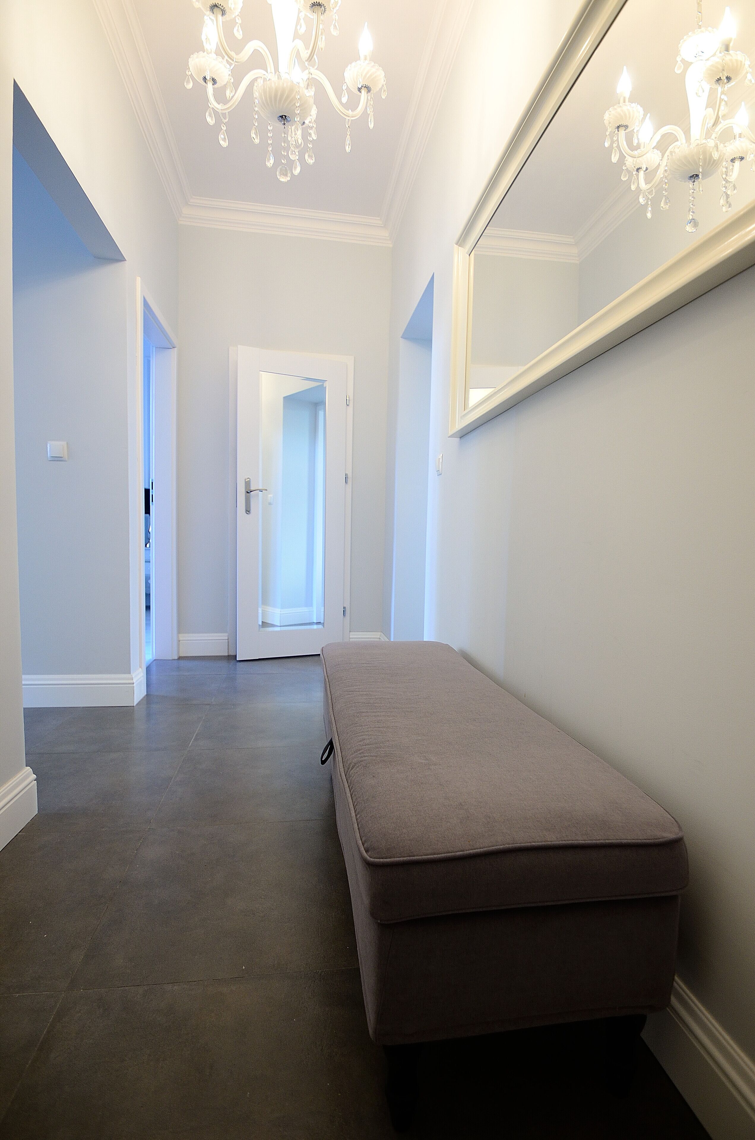 A hallway with a bench, a chandelier, and a large mirror on the wall.