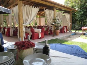 An outdoor dining area with tables set for a meal, covered by a wooden pergola, and surrounded by greenery. - Park Hotel Serenissima (Sacrofano)