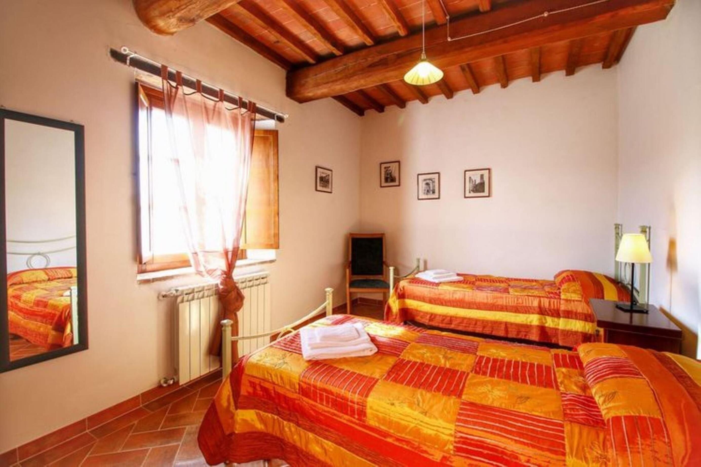 Quarto com duas camas, teto de madeira, janela com cortinas, radiador e quadros na parede.
