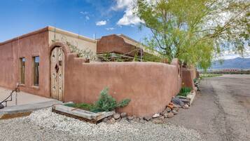 A stucco building with a wooden door, a small garden with rocks and plants, and a clear sky.