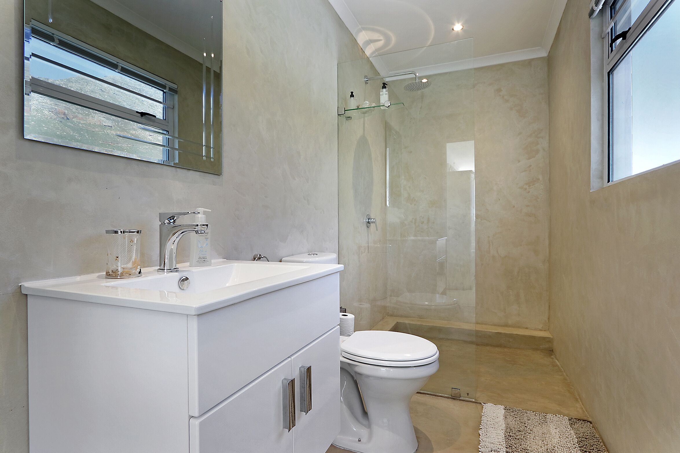 A modern bathroom with a white vanity, a toilet, and a glass-enclosed shower.