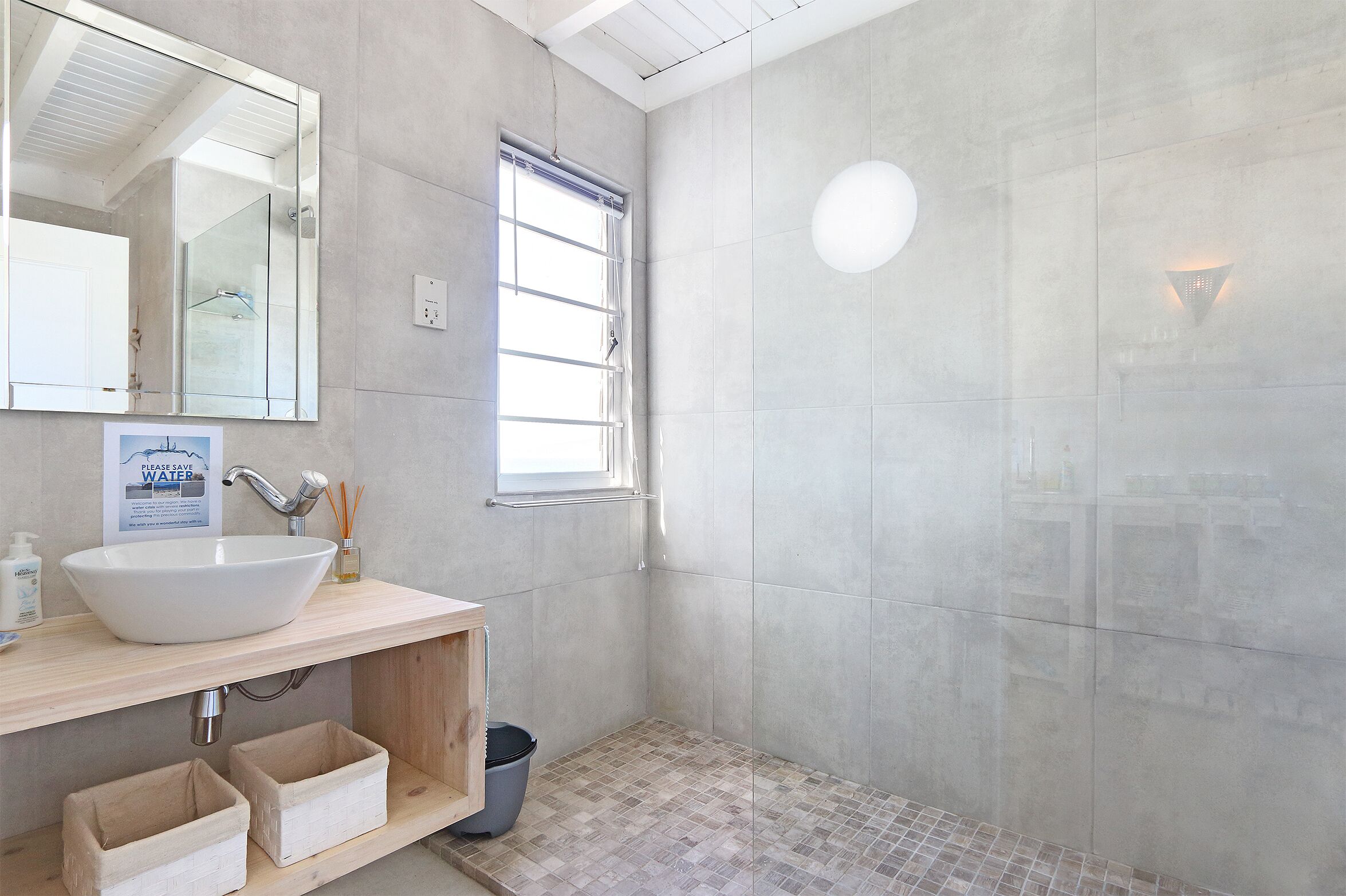 A bathroom with a large mirror, a sink, a shower, and a small window.
