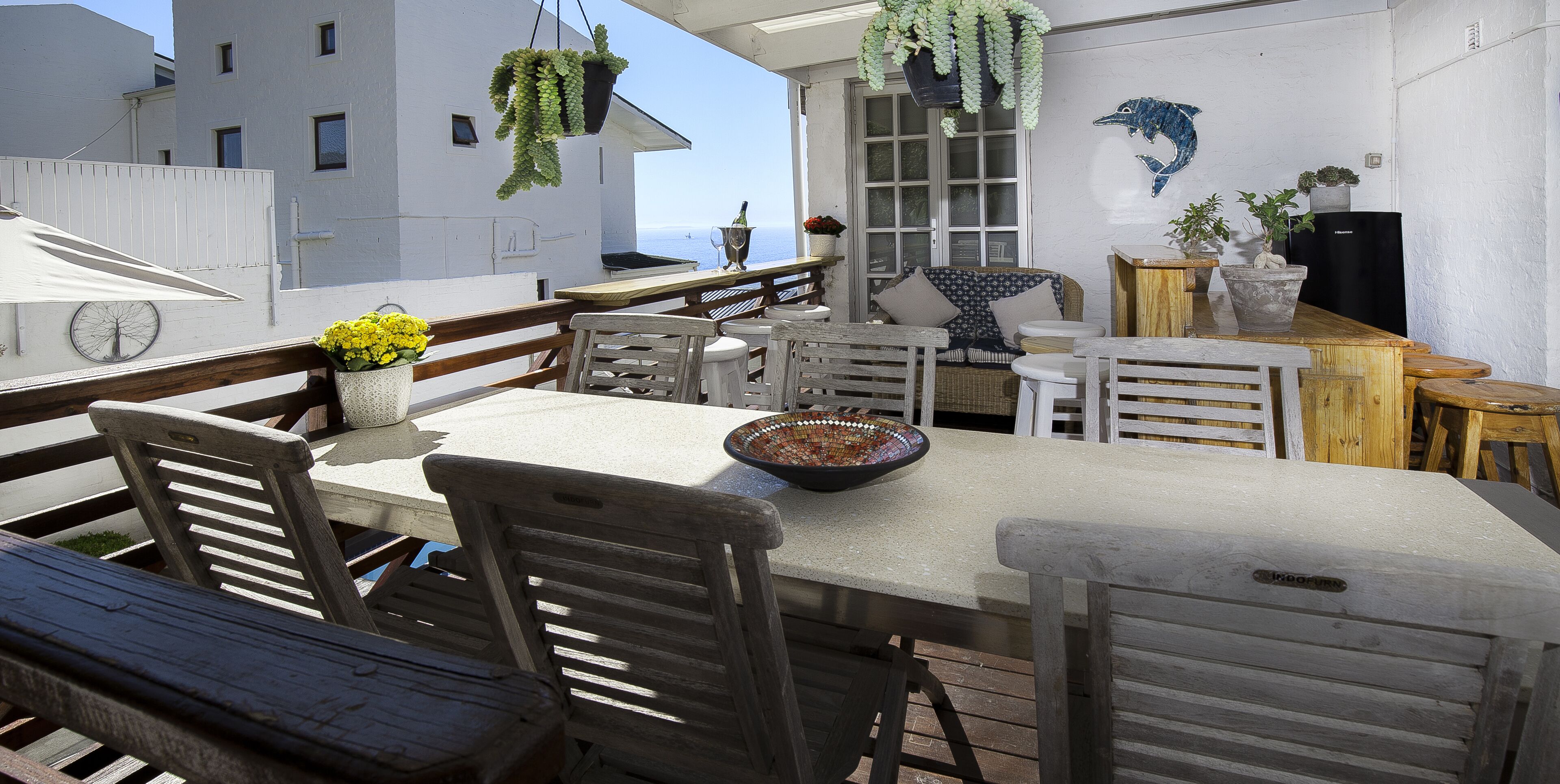 A terrace with a table, chairs, hanging plants, and a view of the sea.