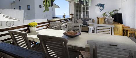 A terrace with a table, chairs, hanging plants, and a view of the sea.