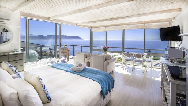 A spacious bedroom with a large bed, a balcony with a view of the ocean, and a television mounted on the wall. - Penguins View Guesthouse (Cape Town)