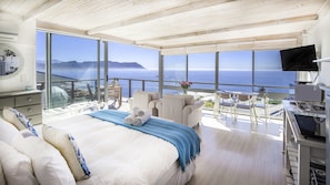 A spacious bedroom with a large bed, a balcony with a view of the ocean, and a television mounted on the wall. - Penguins View Guesthouse (Cape Town)