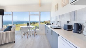 A modern kitchen with large windows, a dining area, and a view of the ocean. - Penguins View Guesthouse (Cape Town)