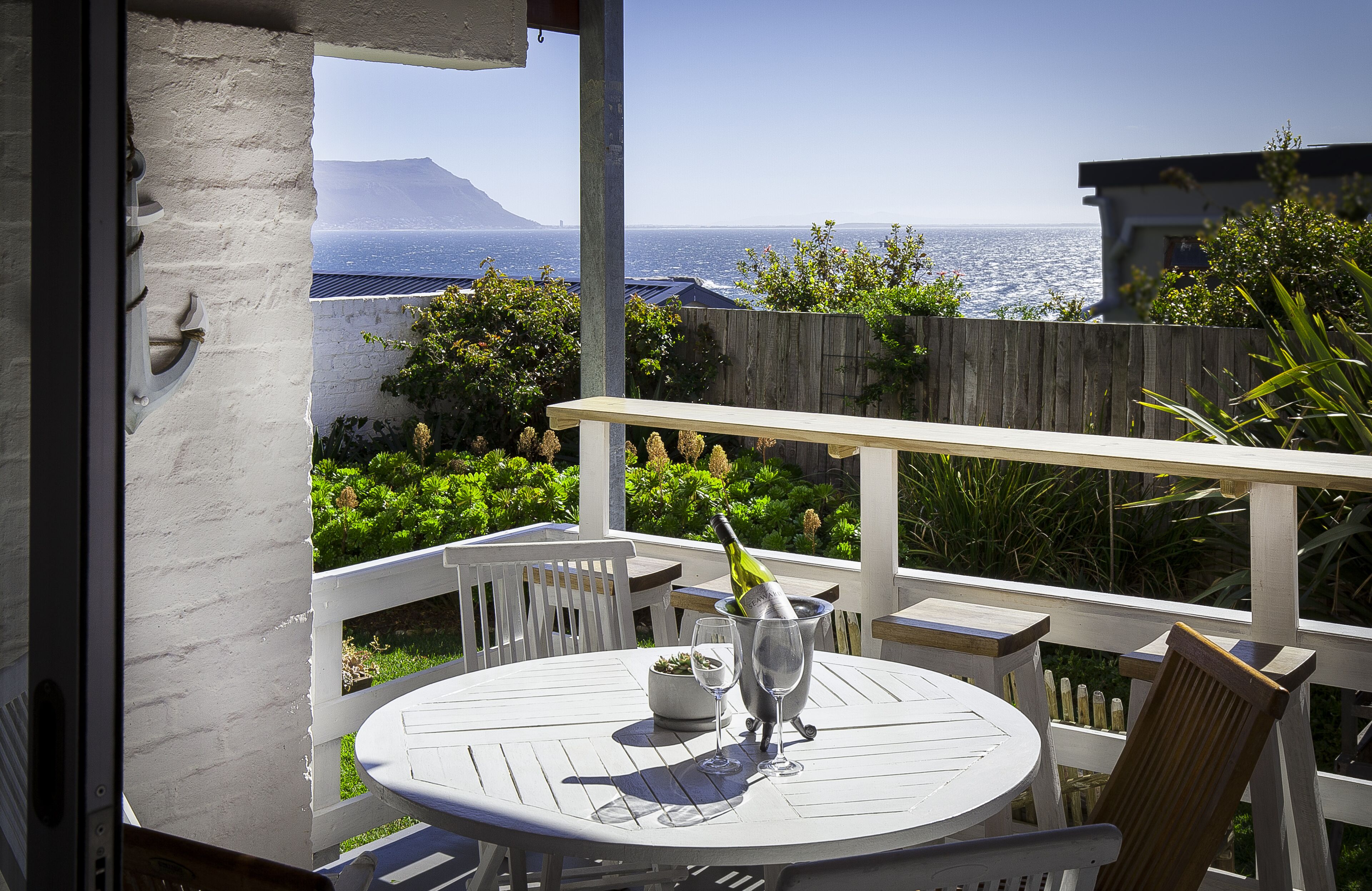 A patio with a table and chairs, a bottle of champagne, and a view of the ocean.