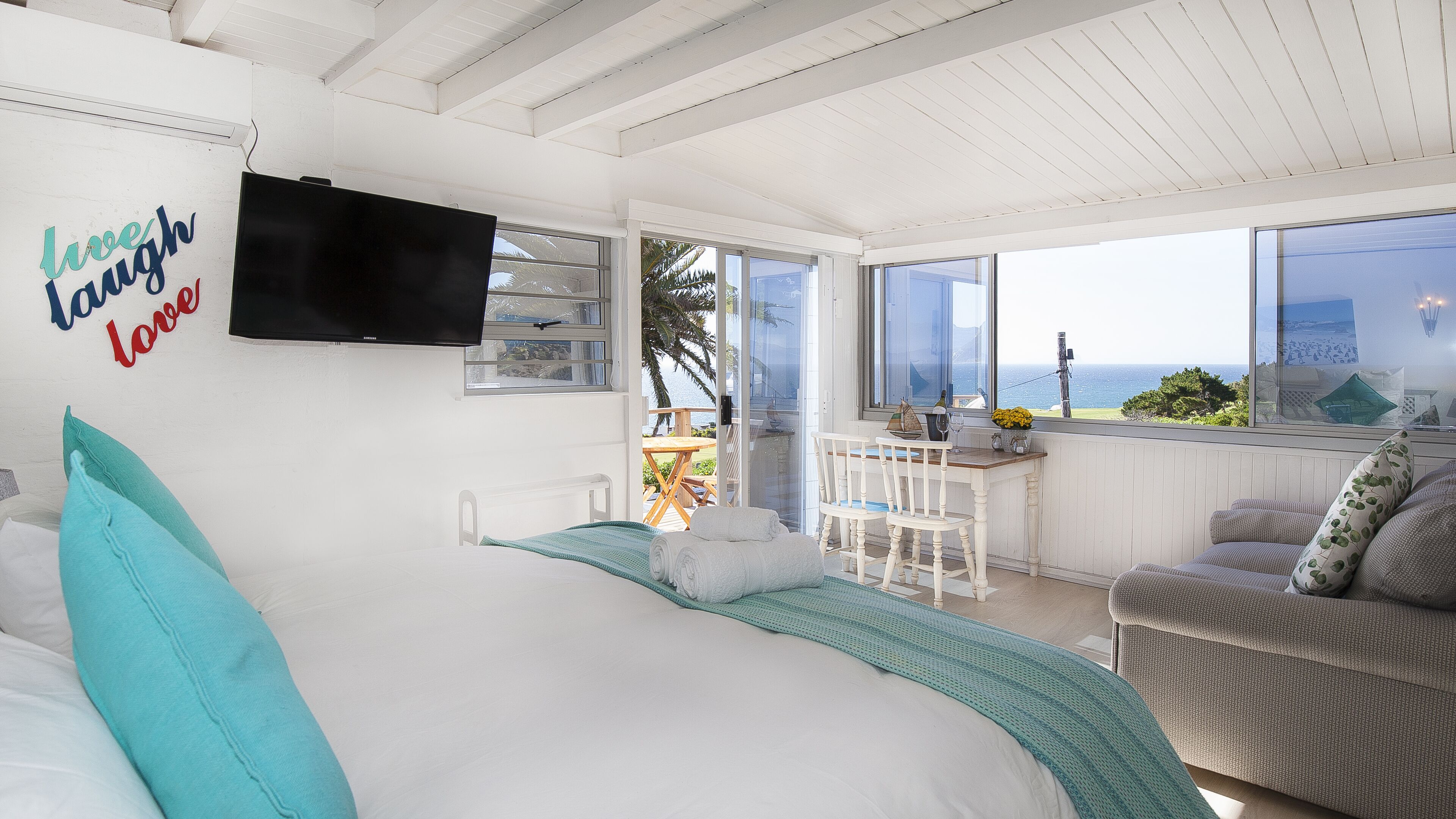 Ein Schlafzimmer mit Bett, Fernseher, einem Balkon mit Meerblick und einem Essbereich mit Tisch und Stühlen.