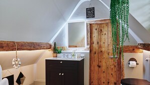 Ein Badezimmer mit Holztür, Waschbecken in Weiß und einer hängenden Pflanze.