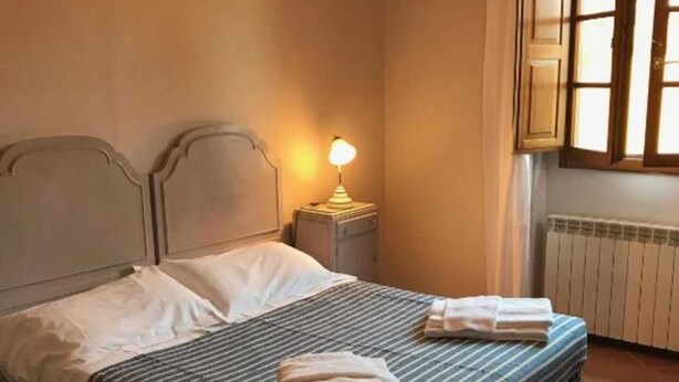 A neatly made bed with striped bedding and two folded towels, a bedside lamp, and a window with curtains. - Frantoio-Large and Beautiful family apartment -Agriturismo San Jacopo (Reggello)