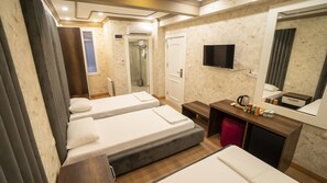 Une chambre d’hôtel avec deux lits simples, un petit bureau avec un miroir, une télévision et un espace douche.