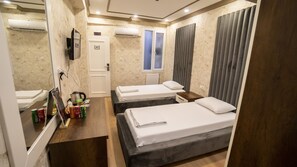 Une chambre d’hôtel avec deux lits, une petite table, un miroir et une fenêtre avec des rideaux.