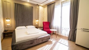Une chambre d’hôtel avec un grand lit, un fauteuil rouge, une petite table ronde et un minibar.