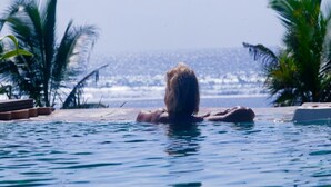 Une personne nage dans une piscine d’où l’on peut admirer l’océan et les palmiers.