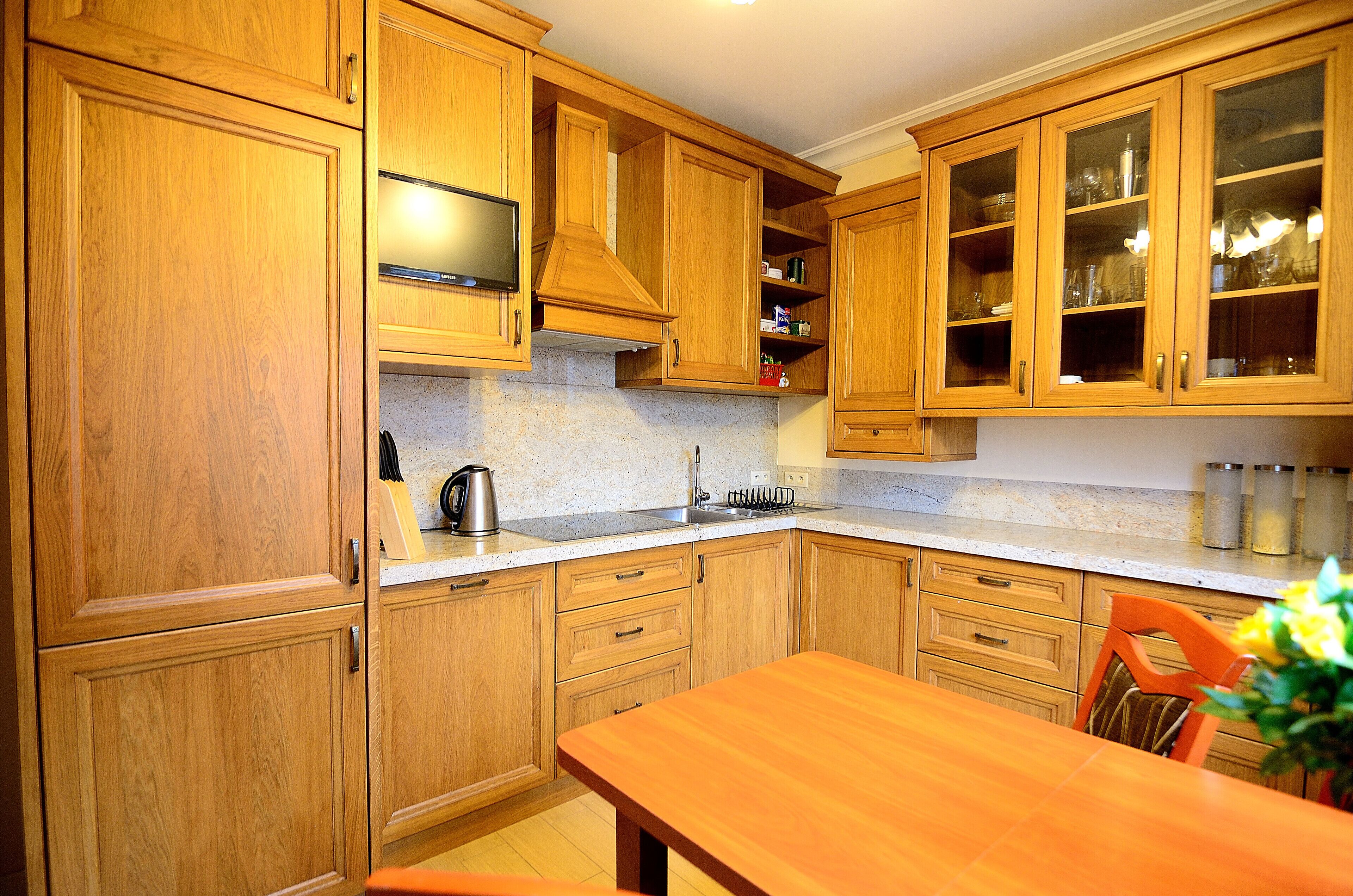 Een keuken met houten kasten, een granieten aanrecht, een roestvrijstalen spoelbak en een eettafel met stoelen.