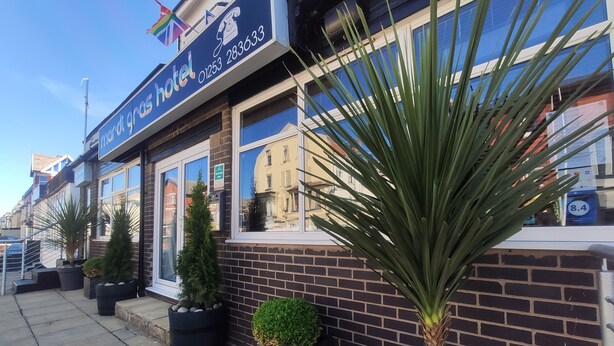 A hotel with a blue signboard, a brick facade, and potted plants along the sidewalk. - Mardi Gras Hotel (Blackpool)