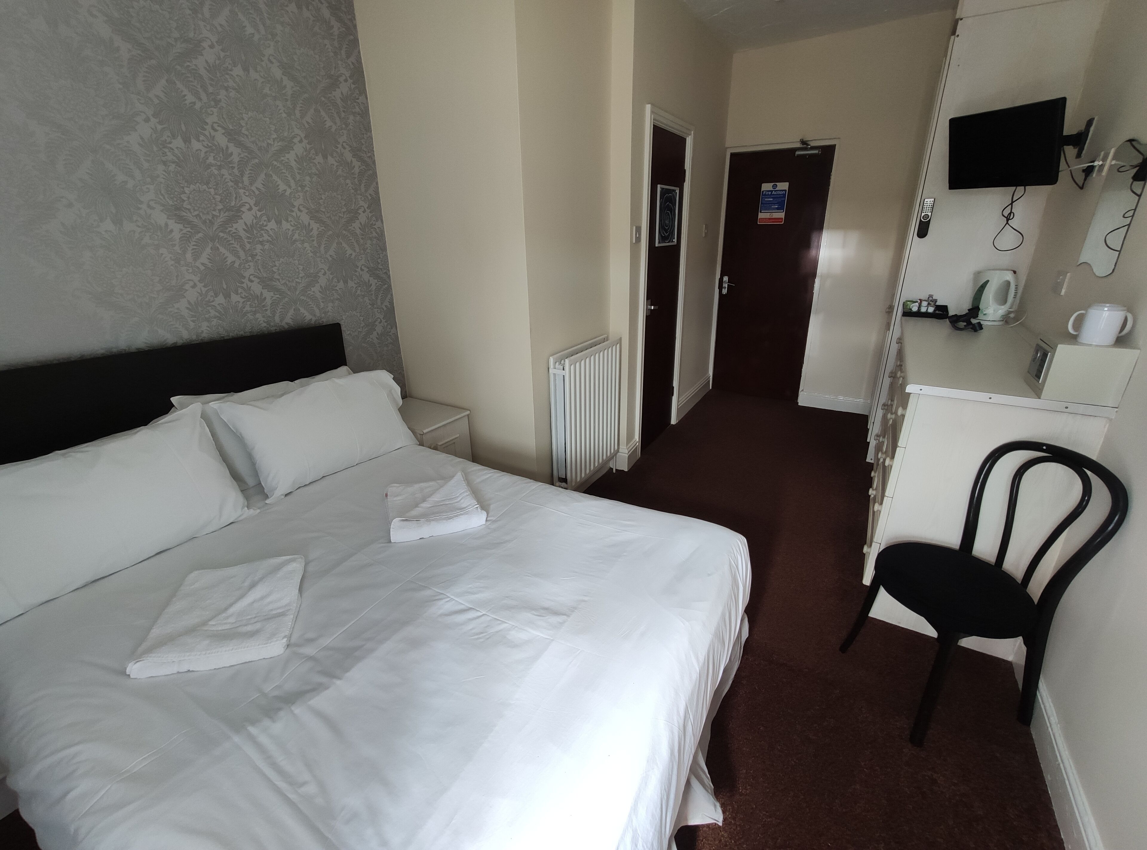 A hotel room with a large bed, a chair, a small table with a kettle, and a TV mounted on the wall.